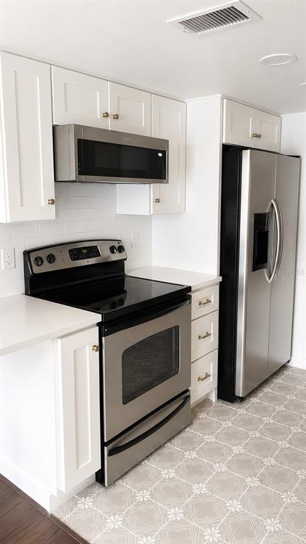 A kitchen features white cabinets, stainless steel appliances, a subway tile backsplash, and patterned flooring — 4611 W NORTH B STREET UNIT 232, TAMPA, FL