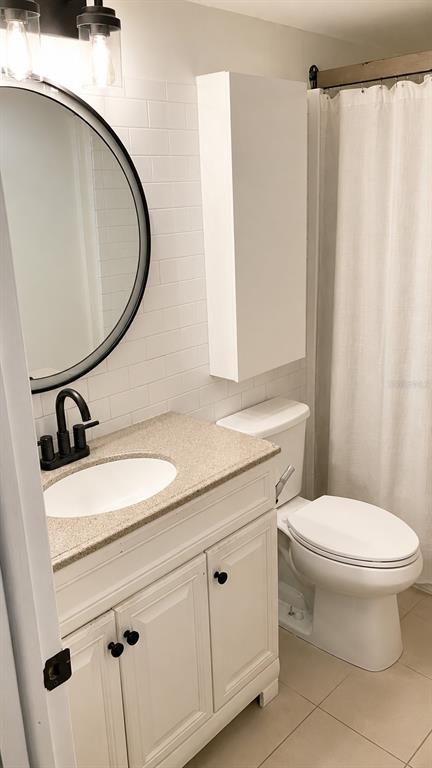 A bathroom features a white vanity with a stone countertop, round mirror, and white subway tile — 4611 W NORTH B STREET UNIT 232, TAMPA, FL