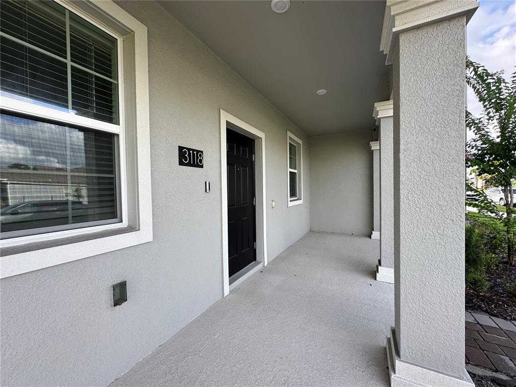 A covered porch features a black front door, a large window, and concrete flooring — 3118 ADDISON BOULEVARD, ST CLOUD, FL