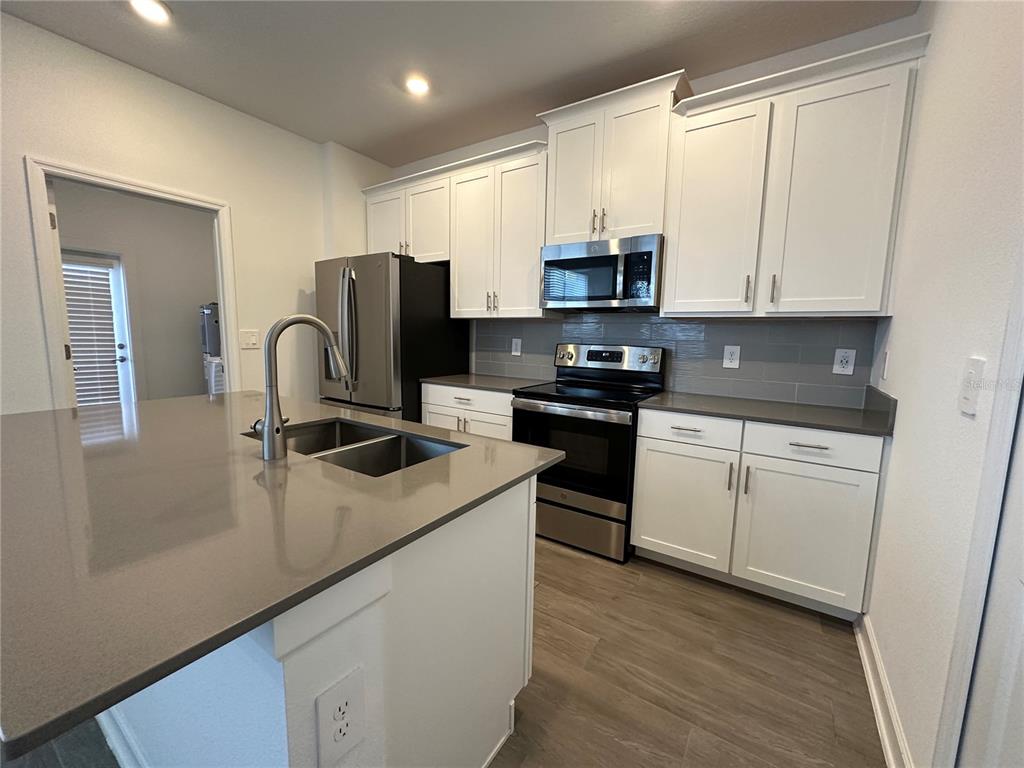 A modern kitchen features white cabinets, stainless steel appliances, and a large gray-topped island — 3118 ADDISON BOULEVARD, ST CLOUD, FL