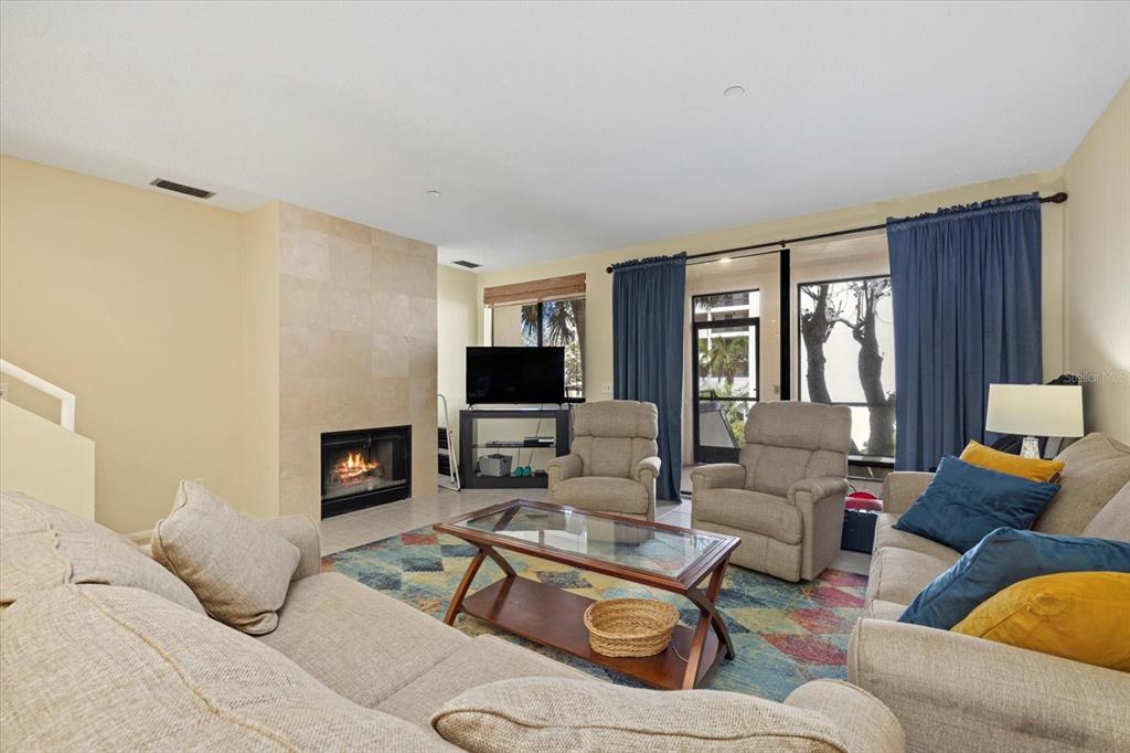 A living room features a tiled fireplace, beige furniture, a glass coffee table, and curtains — 2012 HARBOURSIDE DRIVE UNIT 2102, LONGBOAT KEY, FL