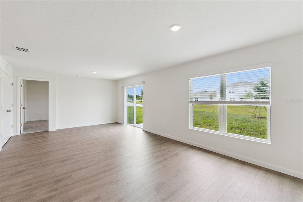 An empty living room features light wood-look flooring, white walls, recessed lighting, and sliding doors — 369 BASS COURT, POINCIANA, FL