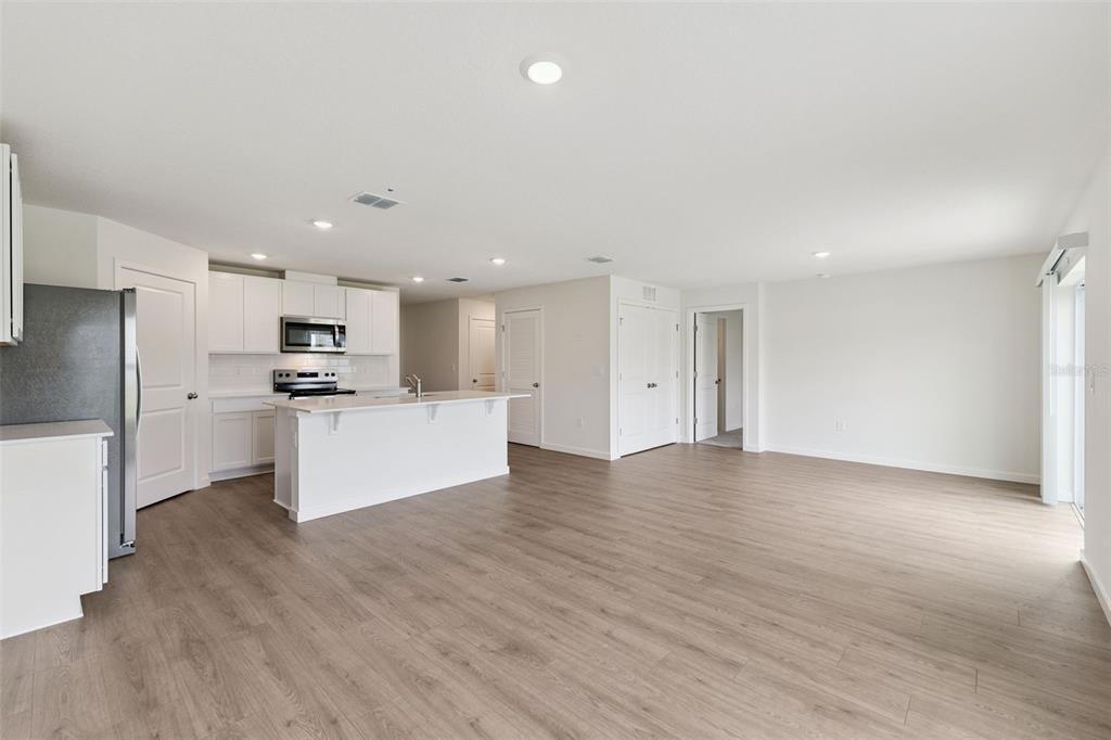 An open-concept kitchen with white cabinets and an island overlooks a spacious living area — 369 BASS COURT, POINCIANA, FL