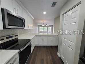 A kitchen with white cabinets, stainless steel appliances, quartz countertops, and dark wood-look flooring — 5903 TOPHER TRAIL UNIT 5903, MULBERRY, FL