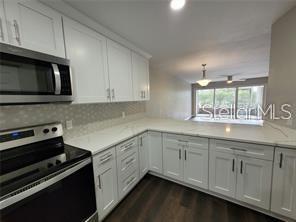 A kitchen with white cabinets, stainless steel appliances, and white countertops overlooks a living area — 5903 TOPHER TRAIL UNIT 5903, MULBERRY, FL