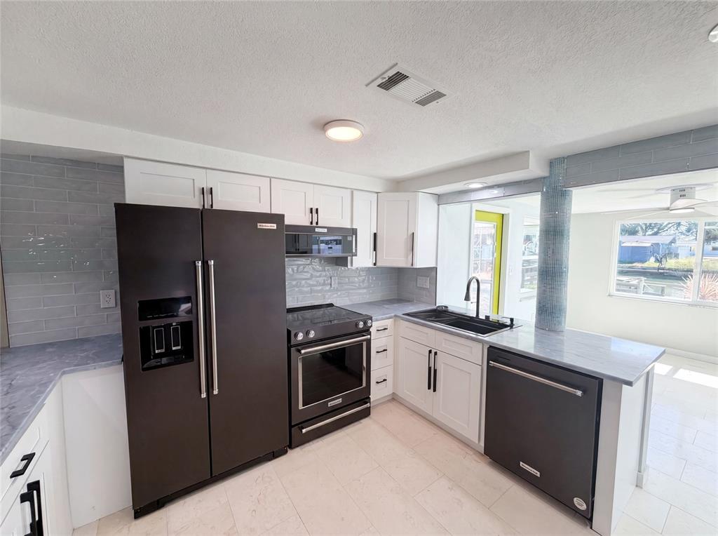 A kitchen features white cabinets, black appliances, gray countertops, and a light-colored tile floor — 13638 EVELANE DRIVE, HUDSON, FL
