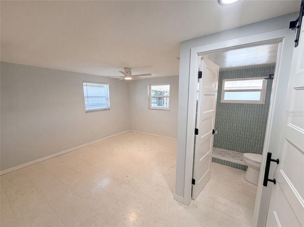 A bedroom with light-colored walls and tile flooring leads into a small tiled bathroom — 13638 EVELANE DRIVE, HUDSON, FL