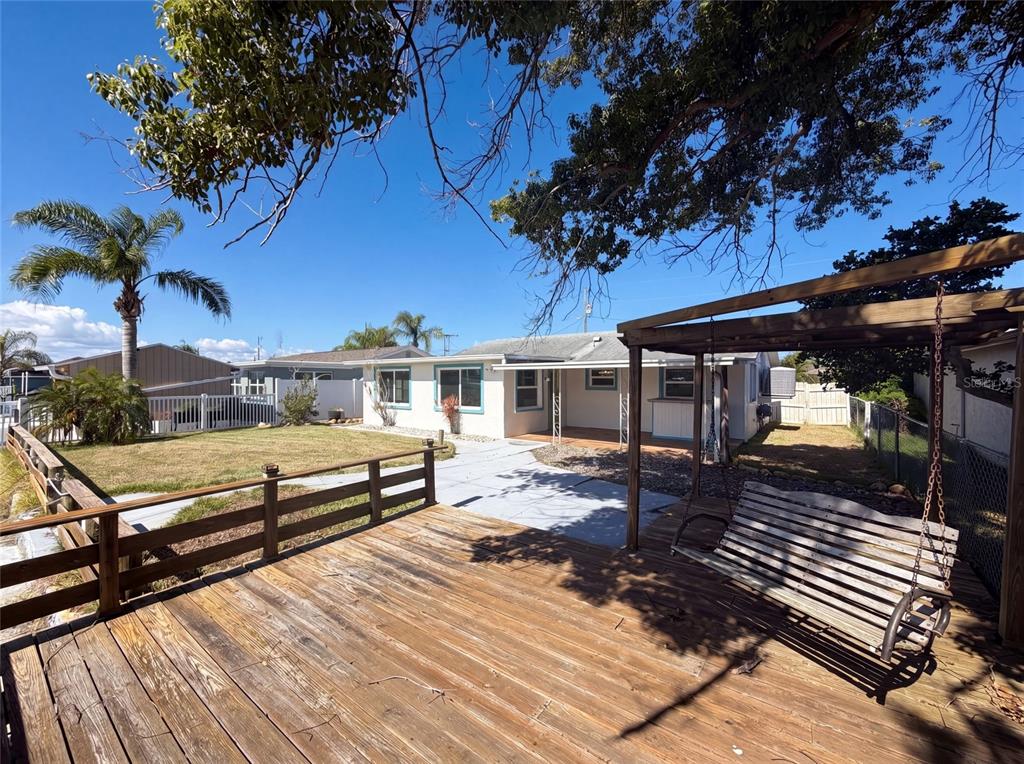 A wooden deck with a hanging swing overlooks a backyard with a patio and house — 13638 EVELANE DRIVE, HUDSON, FL