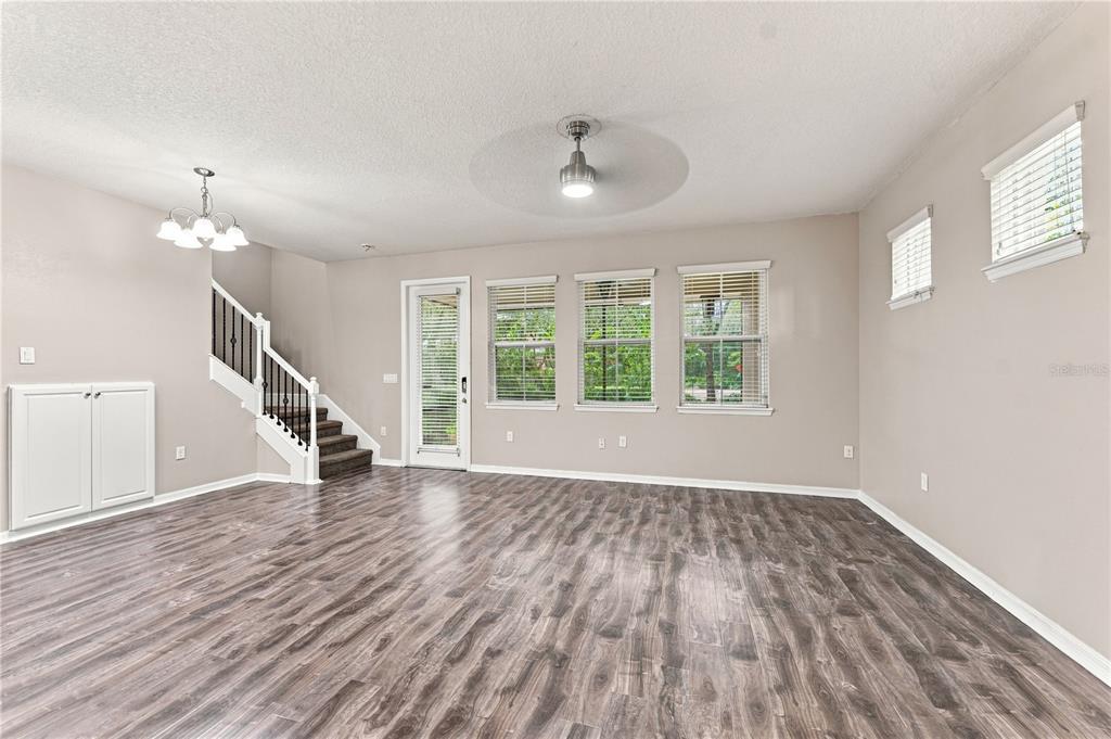 An empty living room features wood-look flooring, a staircase with a railing, and multiple windows — 17013 VILESTA DRIVE, LUTZ, FL