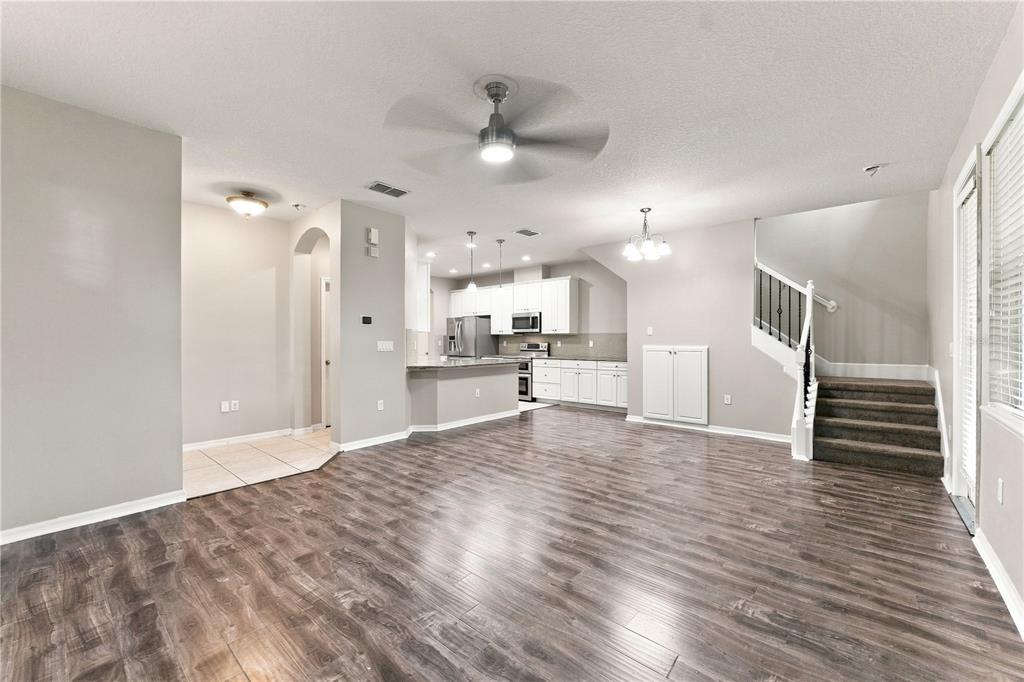 An open-concept living area features wood-look flooring, a kitchen with white cabinets, and stairs — 17013 VILESTA DRIVE, LUTZ, FL