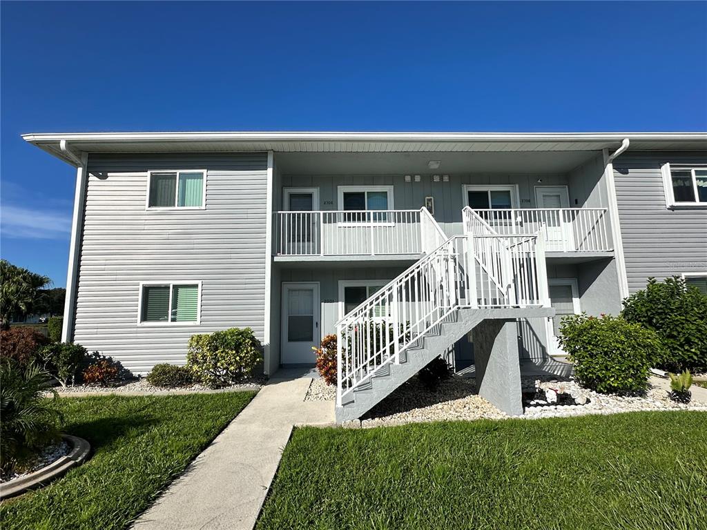 A two-story apartment building features gray siding, white railings, and an exterior staircase — 12274 SW EGRET CIRCLE UNIT 2705, LAKE SUZY, FL