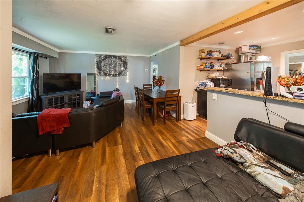 An open-concept living and dining area features wood-look flooring, a black sectional, and kitchen counters — 304 E HYDRANGIA STREET, TAMPA, FL