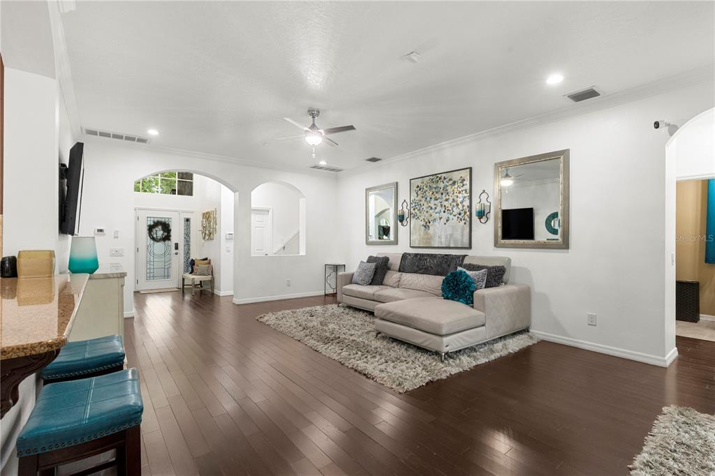 A living room features dark hardwood floors, a sectional sofa, and a large area rug — 6932 GRAY CATBIRD LOOP, WESLEY CHAPEL, FL