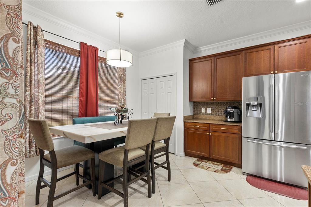 A dining area features a table with chairs, a bench, and wood cabinets near a refrigerator — 6932 GRAY CATBIRD LOOP, WESLEY CHAPEL, FL