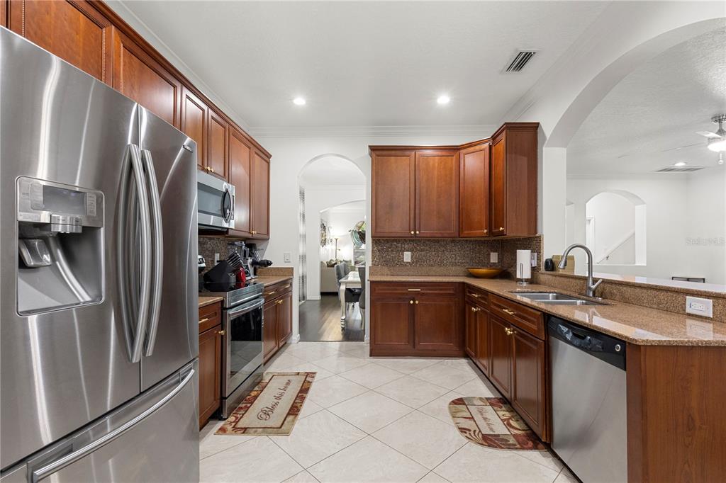A kitchen features cherry wood cabinets, granite countertops, stainless steel appliances, and tile flooring — 6932 GRAY CATBIRD LOOP, WESLEY CHAPEL, FL