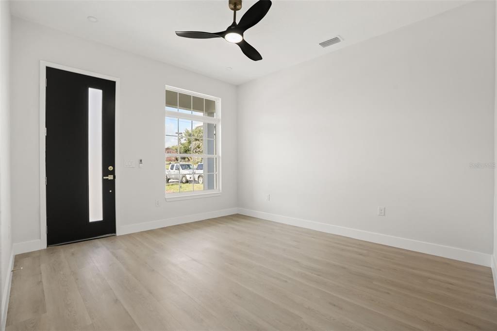 A bright room features light wood-look flooring, white walls, a ceiling fan, and a door — 823 E MCDONALD AVENUE, EUSTIS, FL