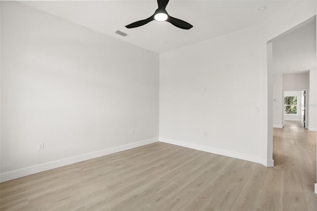 An empty room with white walls, light wood-look flooring, and a modern ceiling fan — 823 E MCDONALD AVENUE, EUSTIS, FL