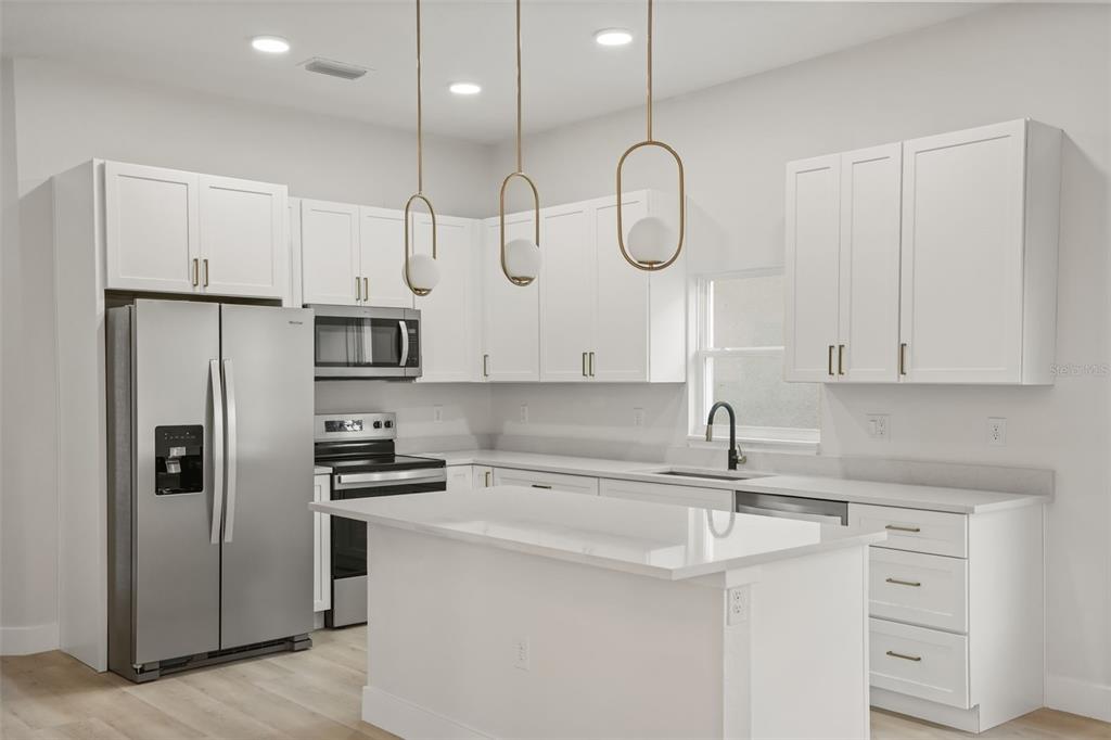 A modern kitchen features white cabinetry, stainless steel appliances, a center island, and pendant lighting — 823 E MCDONALD AVENUE, EUSTIS, FL