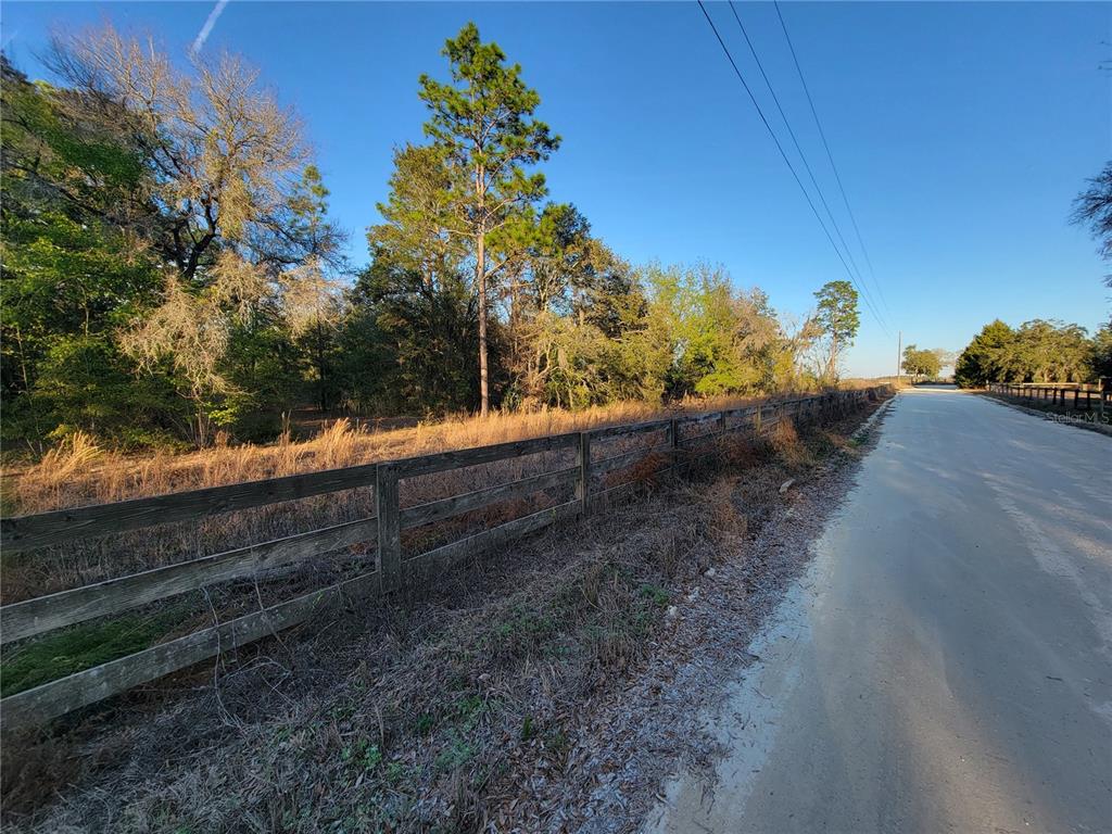 A wooden fence runs along a dirt road beside a wooded lot under clear skies — 0 NE 20TH STREET, WILLISTON, FL