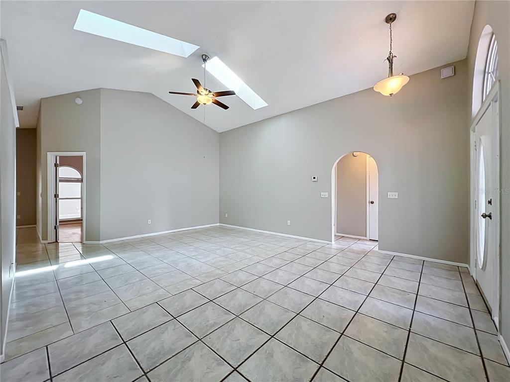 An empty living room features vaulted ceilings, skylights, a ceiling fan, and light-colored tile flooring — 1365 CRAWFORD DRIVE, APOPKA, FL