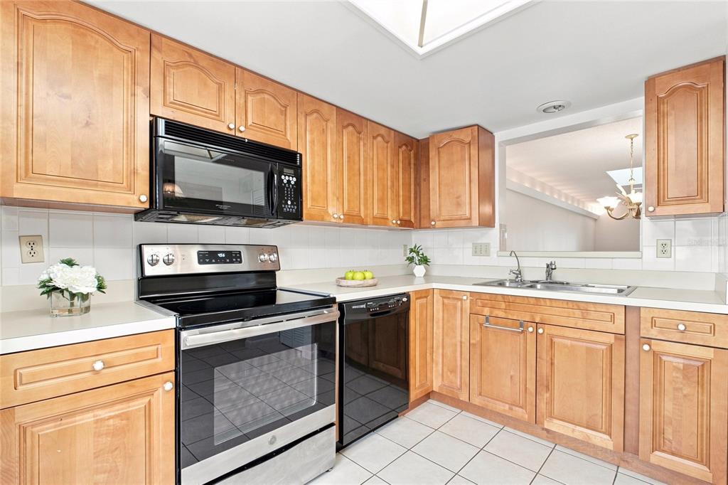 A kitchen features light wood cabinets, stainless steel appliances, white tile backsplash, and white countertops — 3370 STONEHAVEN COURT W UNIT B, PALM HARBOR, FL