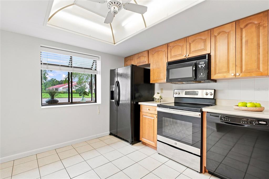 A kitchen with light wood cabinets, black appliances, tile flooring, and a window overlooking outdoors — 3370 STONEHAVEN COURT W UNIT B, PALM HARBOR, FL