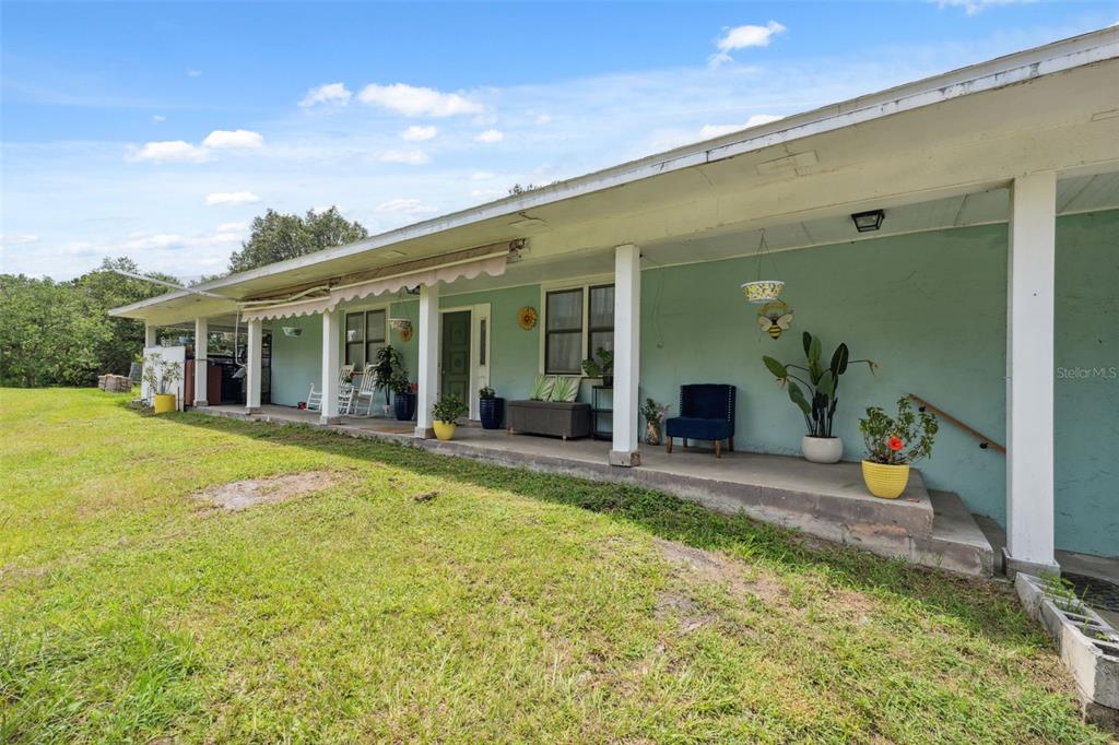 A long, covered porch runs along the front of a light green, single-story house — 4527 REDCOAT DRIVE, WESLEY CHAPEL, FL