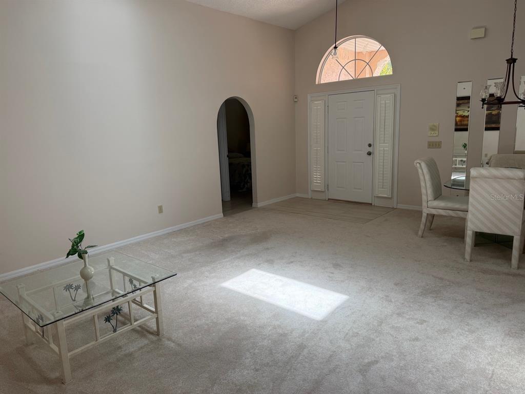 A living room with beige carpet, a glass coffee table, and an arched doorway — 540 CEDAREDGE DRIVE, NEW SMYRNA BEACH, FL