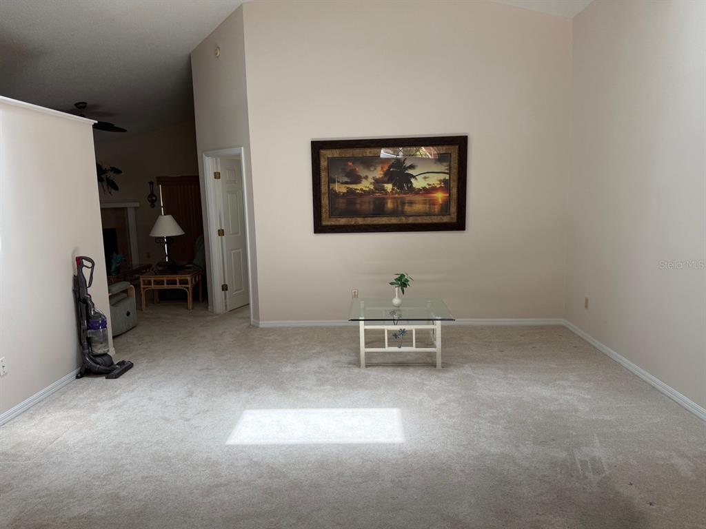A carpeted living room features a glass coffee table, a framed landscape painting, and vaulted ceilings — 540 CEDAREDGE DRIVE, NEW SMYRNA BEACH, FL