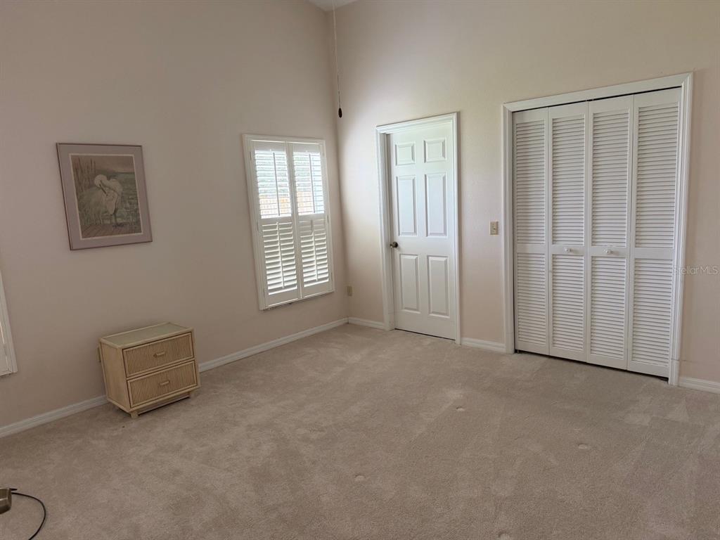 A bedroom features beige carpet, a small wicker nightstand, a window with shutters, and closets — 540 CEDAREDGE DRIVE, NEW SMYRNA BEACH, FL