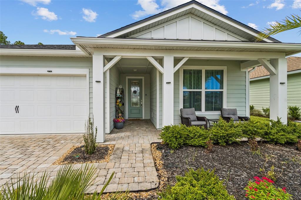 A light green house features a paved walkway, a white garage door, and a covered porch — 217 ETHEREAL SQUARE, YULEE, FL