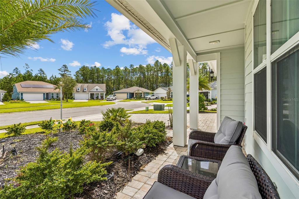 A covered front porch features wicker chairs and a view of a suburban residential street — 217 ETHEREAL SQUARE, YULEE, FL