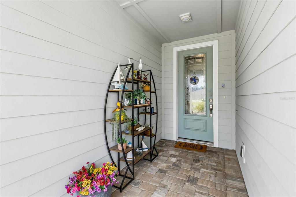 A covered front porch features a light blue door, a metal shelving unit, and pavers — 217 ETHEREAL SQUARE, YULEE, FL