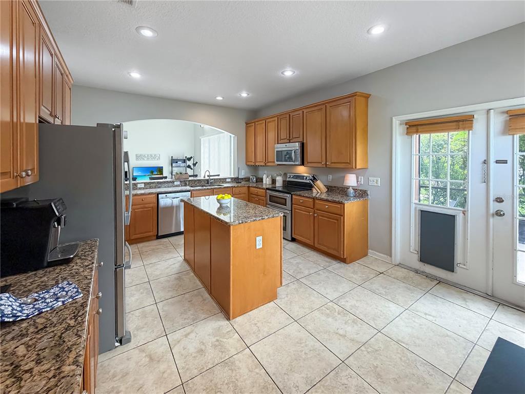 A kitchen with wood cabinets, granite countertops, a center island, and tile flooring — 10172 WINDERMERE CHASE BOULEVARD, GOTHA, FL