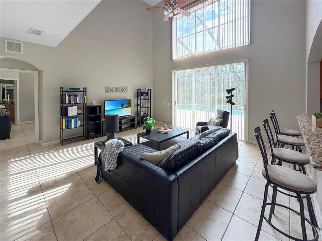 A living room with high ceilings, tile floors, a black sofa, and a sliding glass door — 10172 WINDERMERE CHASE BOULEVARD, GOTHA, FL
