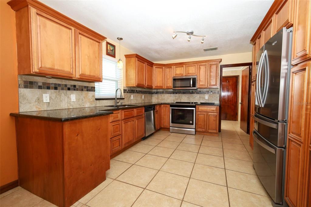 A kitchen features wood cabinets, dark granite countertops, stainless steel appliances, and tiled flooring — 1534 PEREZ STREET, ORLANDO, FL