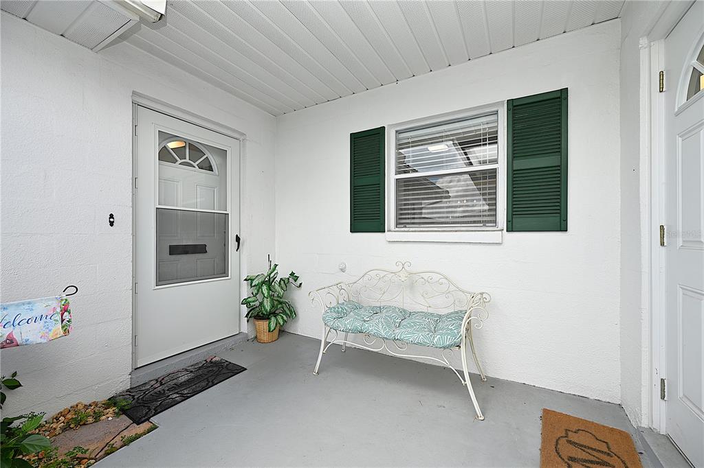 A white-walled front porch features a metal bench, a potted plant, and a welcome flag — 3535 AMITY AVENUE UNIT 3535, LAKELAND, FL