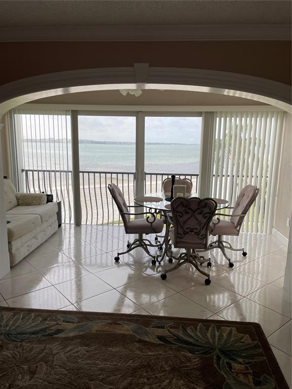 A dining area with a glass table and chairs sits before a balcony overlooking water — 895 S GULFVIEW BOULEVARD UNIT 303, CLEARWATER BEACH, FL