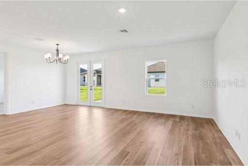 An empty room with light wood flooring, white walls, a chandelier, and glass patio doors — 3173 SAILHOUSE DRIVE, ST CLOUD, FL