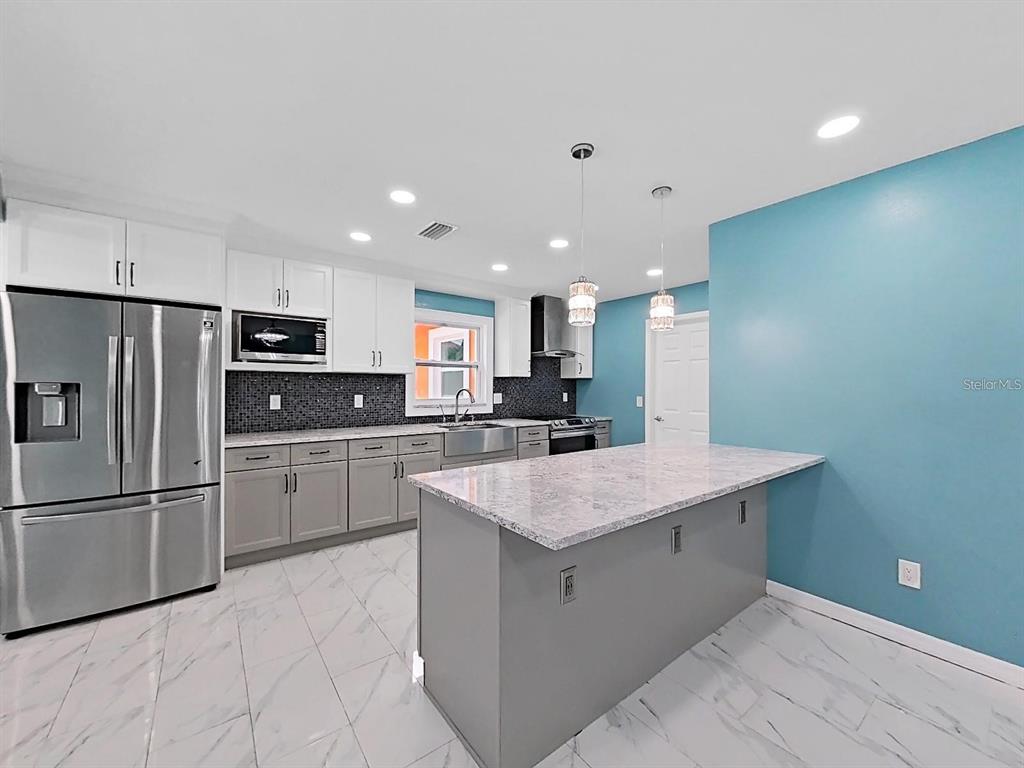 A kitchen features gray lower cabinets, white upper cabinets, a marble island, and blue walls — 1613 33RD STREET SE, RUSKIN, FL
