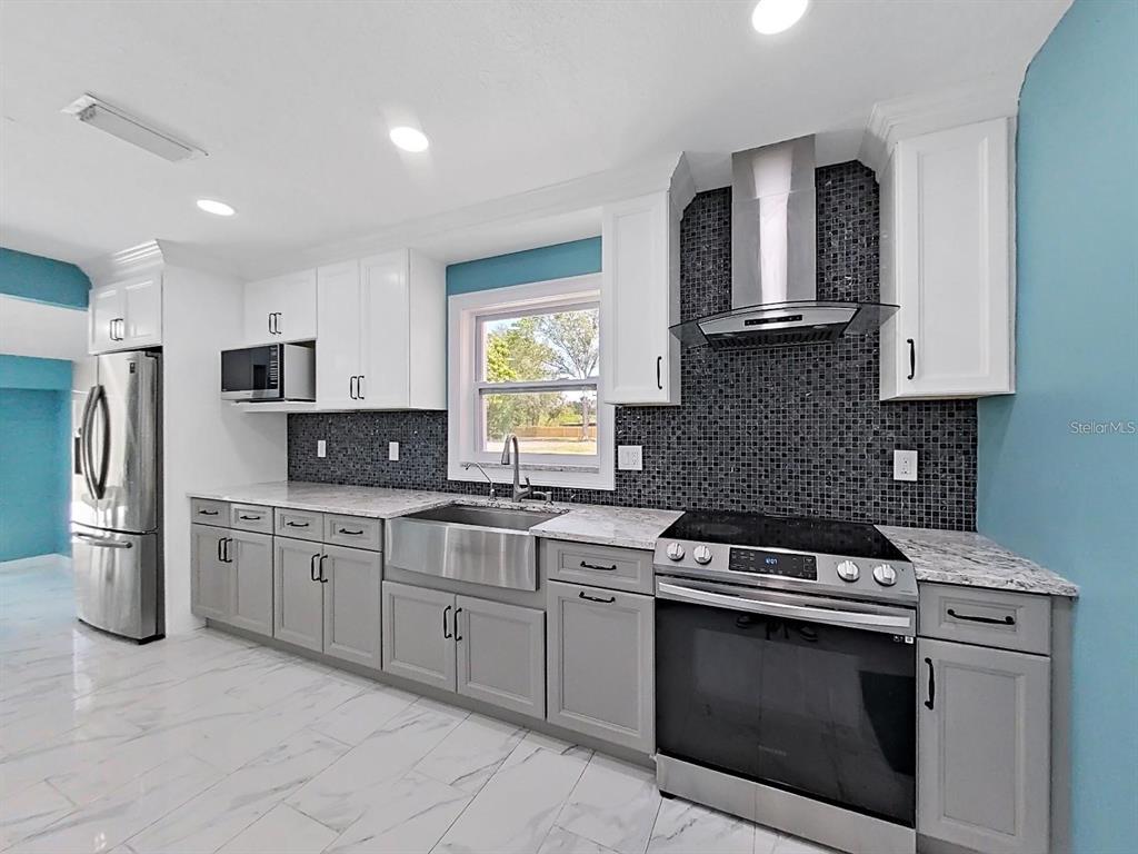 A kitchen features gray lower cabinets, white upper cabinets, a farmhouse sink, and tiled backsplash — 1613 33RD STREET SE, RUSKIN, FL