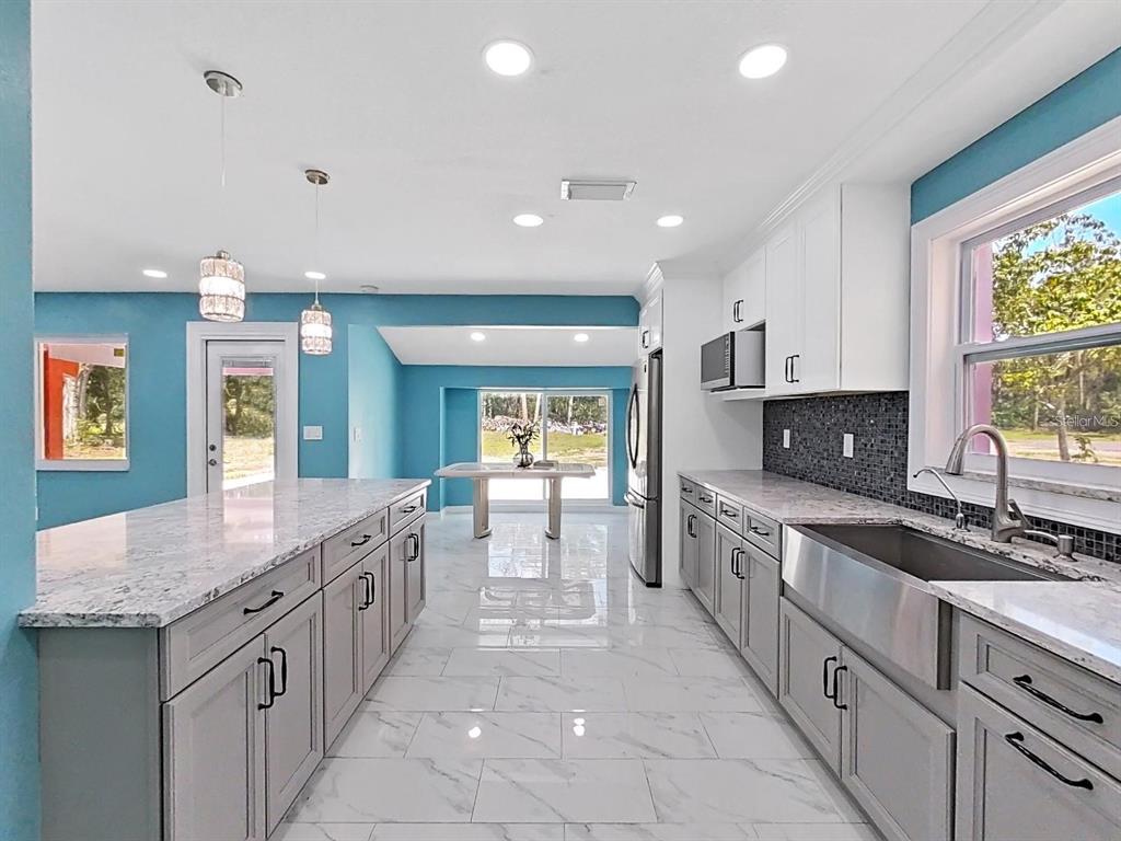 A modern kitchen features gray cabinets, white marble countertops, a farmhouse sink, and blue walls — 1613 33RD STREET SE, RUSKIN, FL
