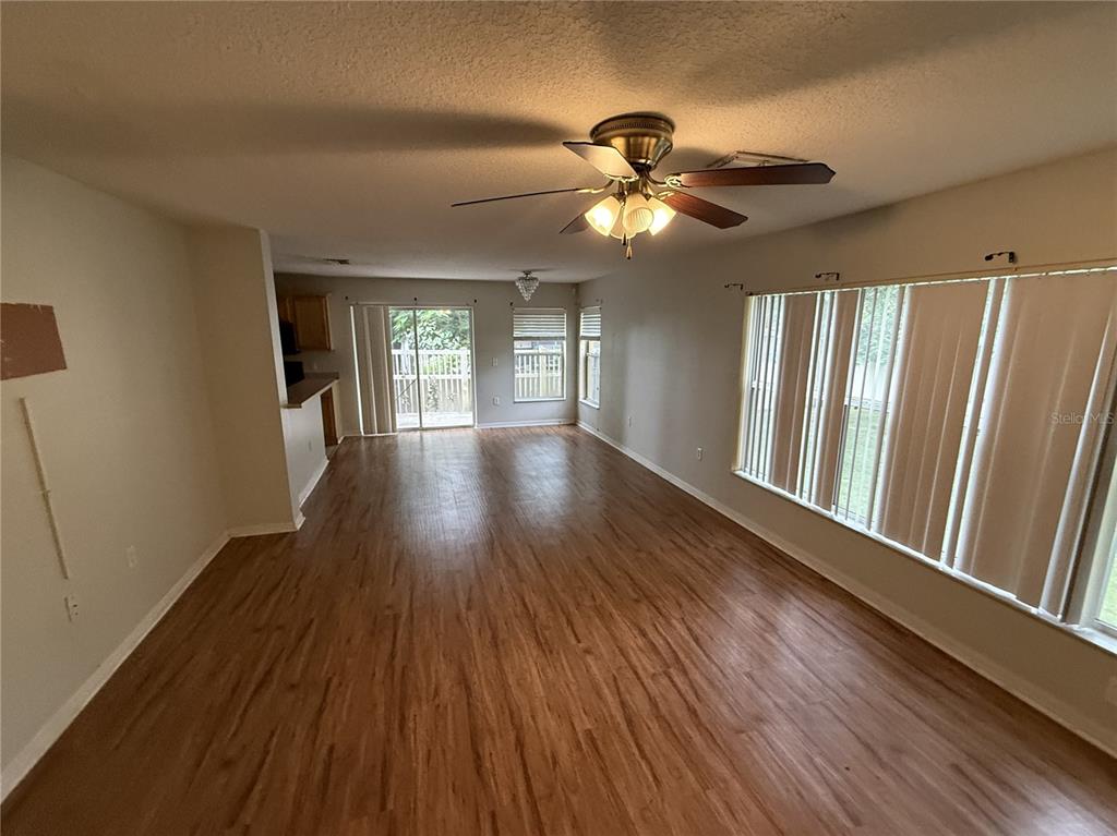 An open-concept living area features wood-look flooring, a ceiling fan, and large windows with blinds — 4521 LIMERICK DRIVE, TAMPA, FL
