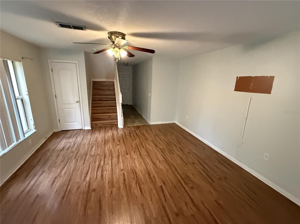 An empty living room features wood-look flooring, a ceiling fan, and a staircase — 4521 LIMERICK DRIVE, TAMPA, FL