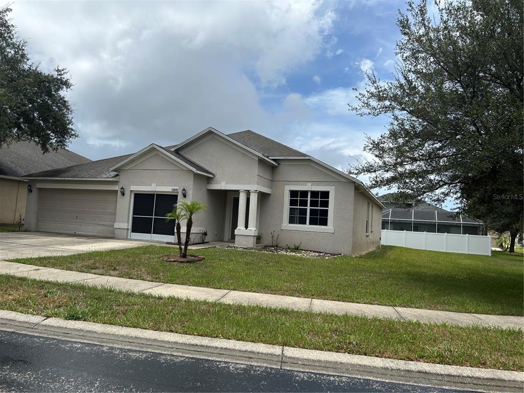 A single-story house with a beige stucco exterior, a two-car garage, and a front lawn — 13042 HAVERHILL DRIVE, SPRING HILL, FL