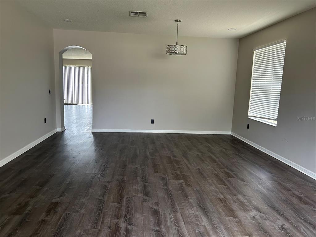 An empty room with dark wood-look flooring, light gray walls, and a decorative pendant light — 13042 HAVERHILL DRIVE, SPRING HILL, FL