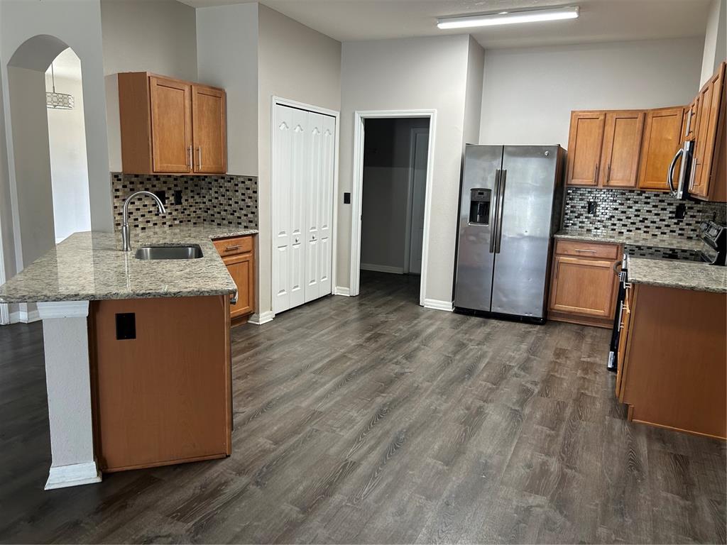 A kitchen features wood cabinets, granite countertops, stainless steel appliances, and dark wood-look flooring — 13042 HAVERHILL DRIVE, SPRING HILL, FL