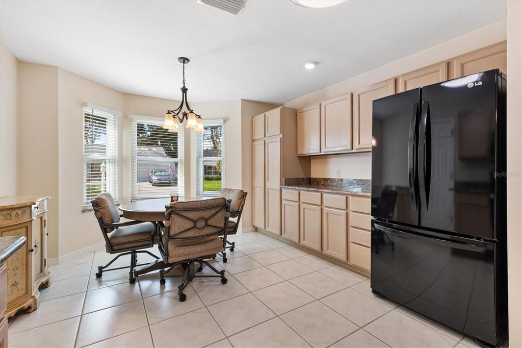 A kitchen with light wood cabinets, a black refrigerator, and a dining area with windows — 915 VENTURA DRIVE, LADY LAKE, FL