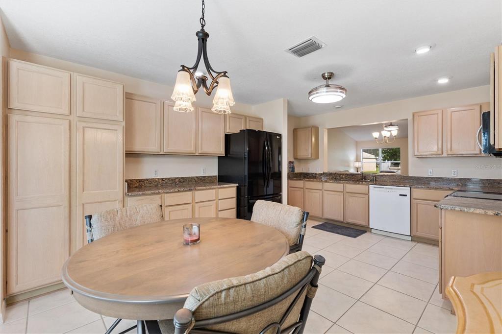 A kitchen with light wood cabinets, granite countertops, a black refrigerator, and a round dining table — 915 VENTURA DRIVE, LADY LAKE, FL
