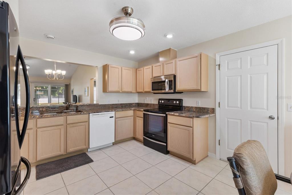 A kitchen with light wood cabinets, granite countertops, white appliances, and beige tile flooring — 915 VENTURA DRIVE, LADY LAKE, FL